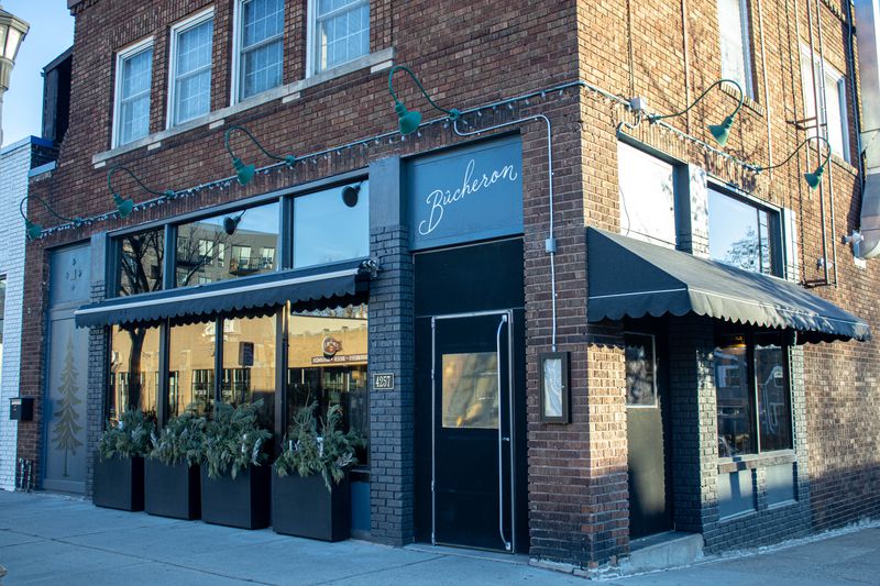 The exterior of a brown brick building with black awnings and a sign that reads “Bûcheron” in gold script. 