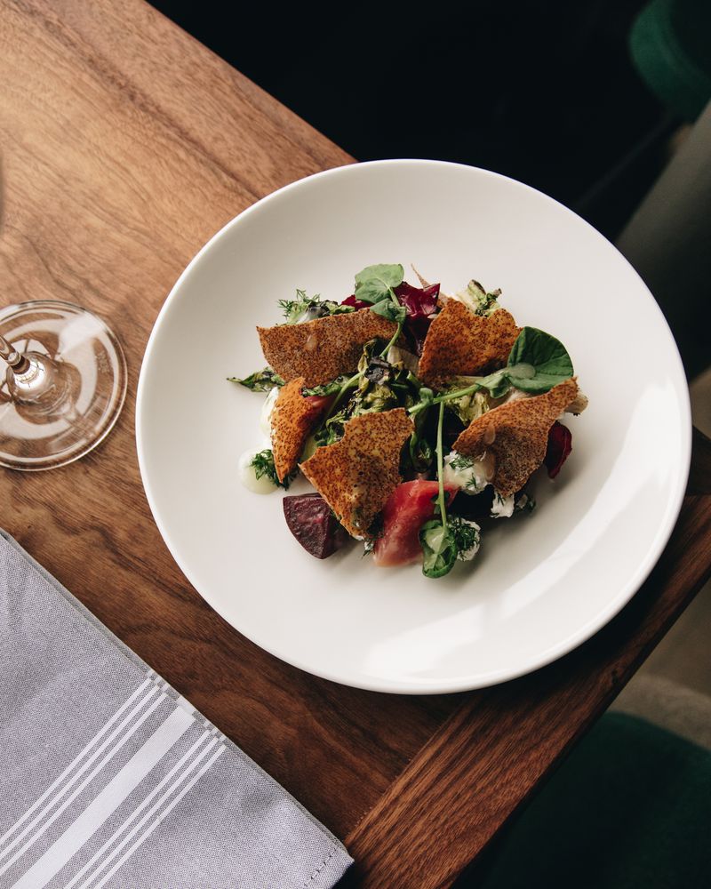 A chicory salad with greens and hunks of roast beets on a white plate on top of a wooden table. 