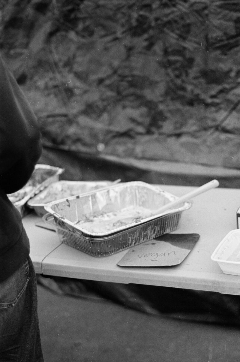 An empty tin catering tray sits on a white folding table with a sign that reads “vegan” next to it.