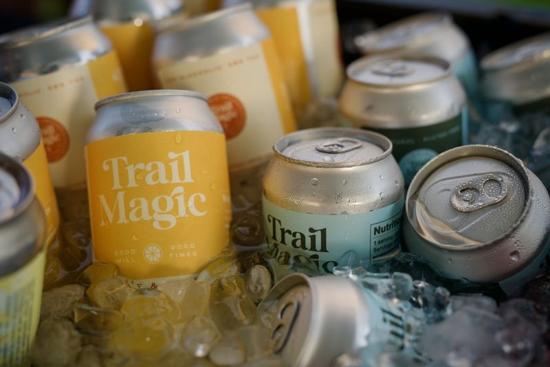 An assortment of cans, some yellow and some light blue, all reading “Trail Magic,” floating in a cooler of ice. 