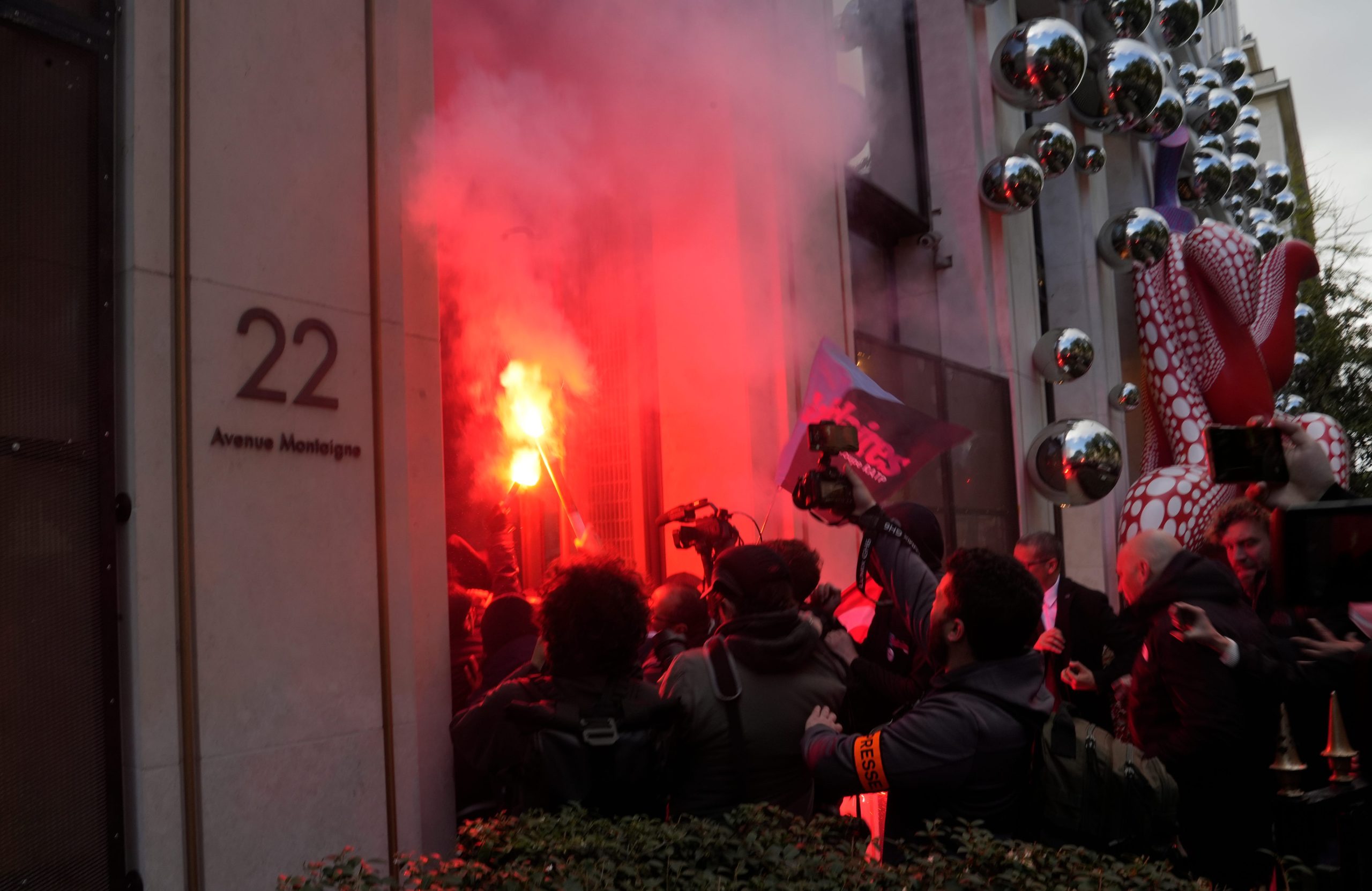 A group of protesters with flares and recording equipment pushing their way into LVMH's headquarters.