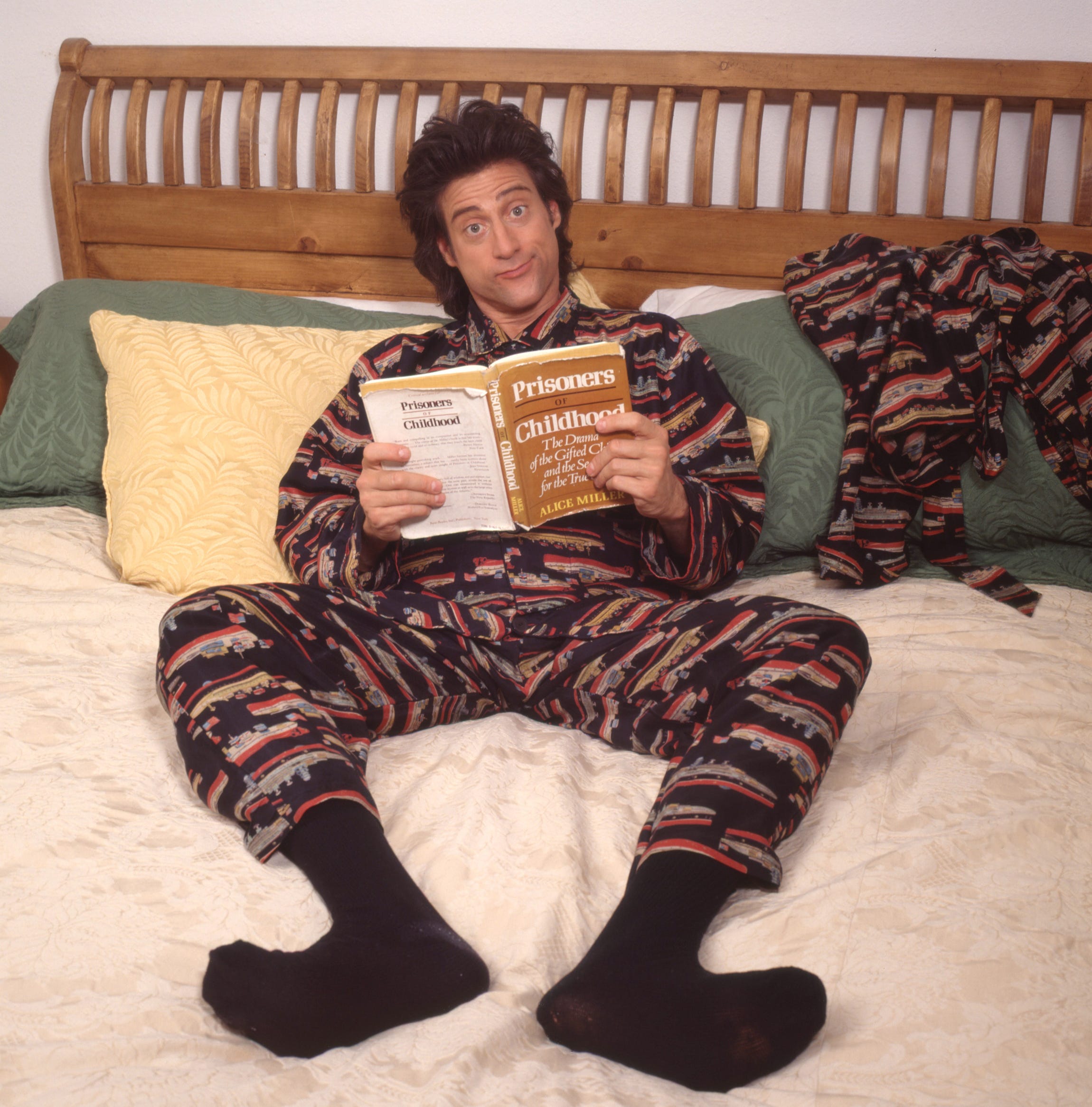 Richard Lewis in pajamas in bed holding a book