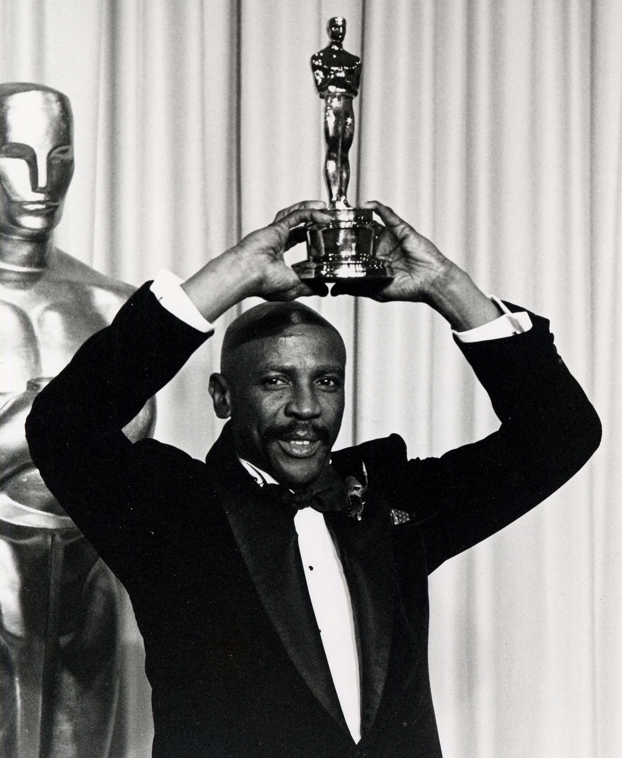 Louis Gossett Jr. in a tuxedo holding his Oscar over his head