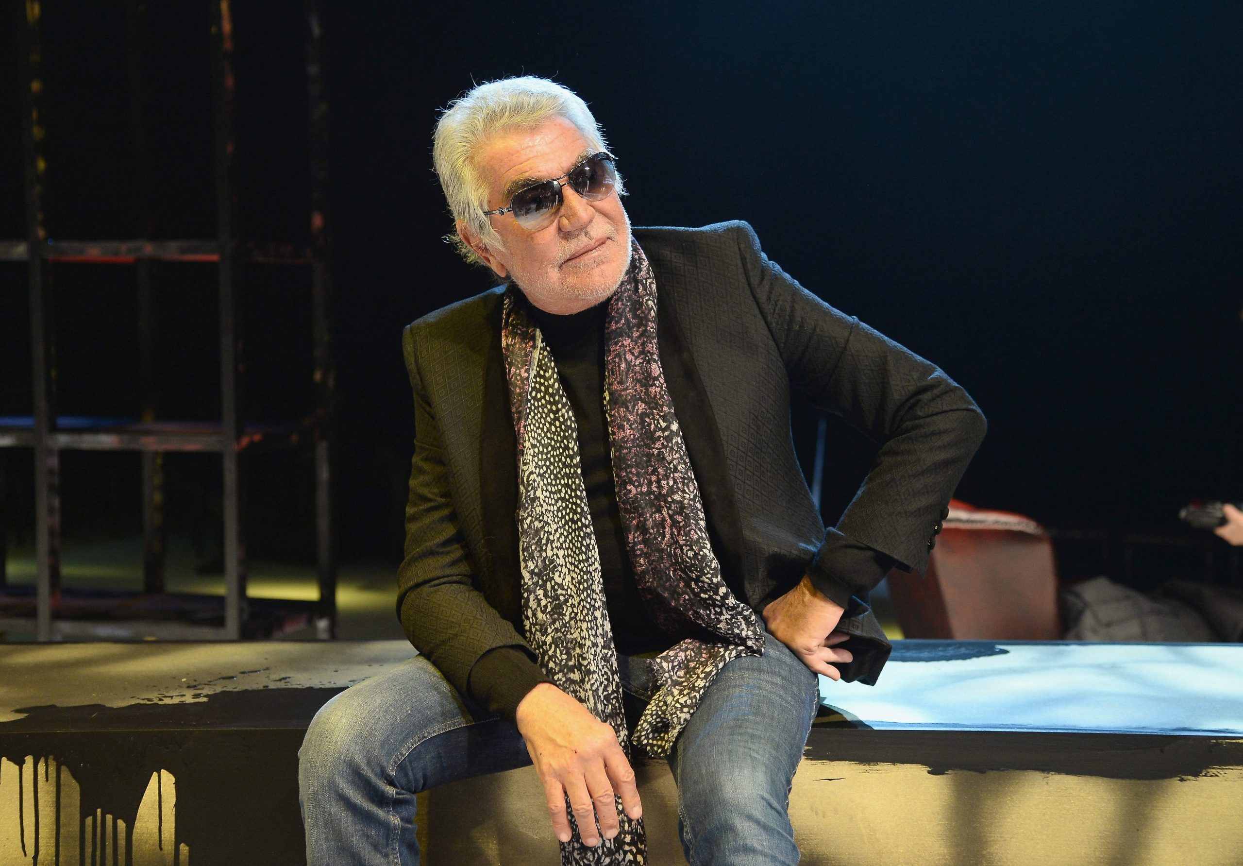 Roberto Cavalli sitting down wearing a jacket and scarf