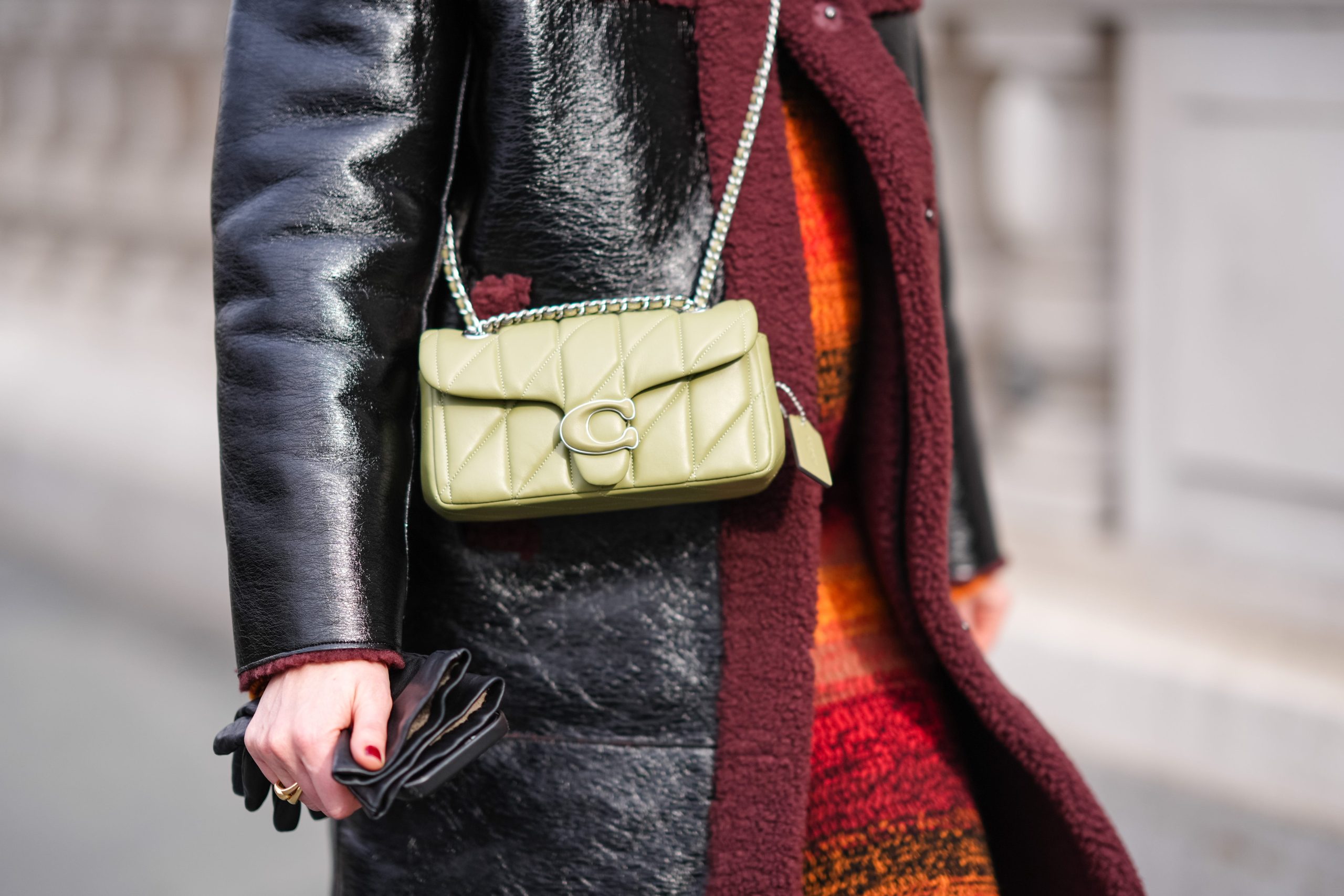 Person wearing crossbody lime green coach bag over leather coat