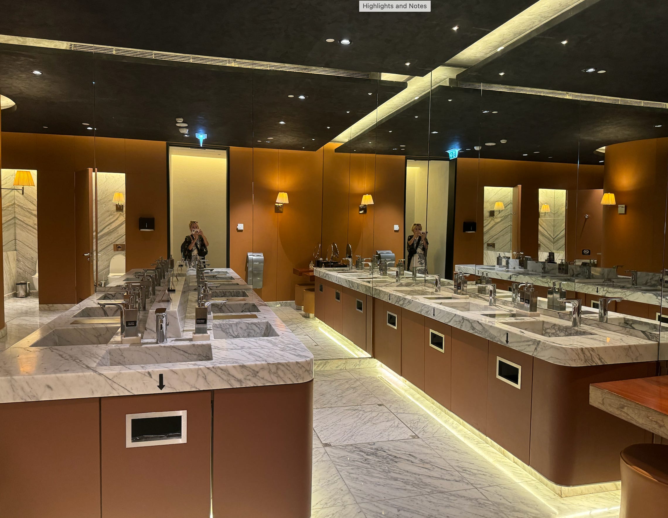 Large bathroom with numerous marble sinks in front of mirrors 