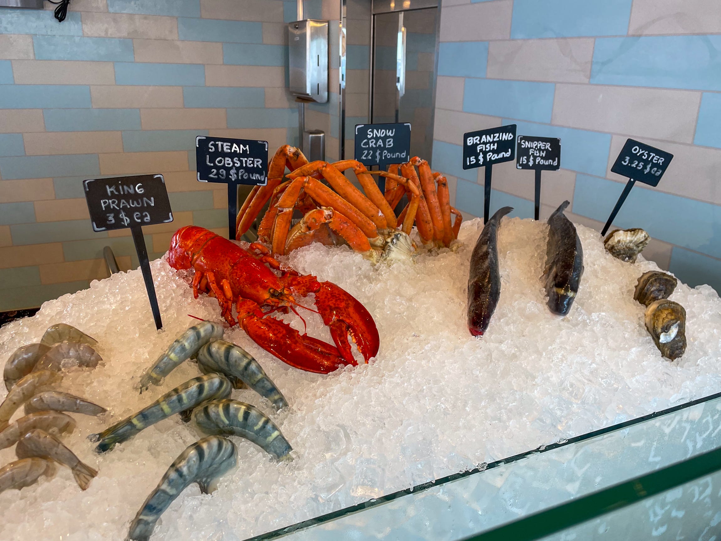 King prawns, lobster, snow crab, branzino fish, snipper fish, and oysters on ice with price tags.