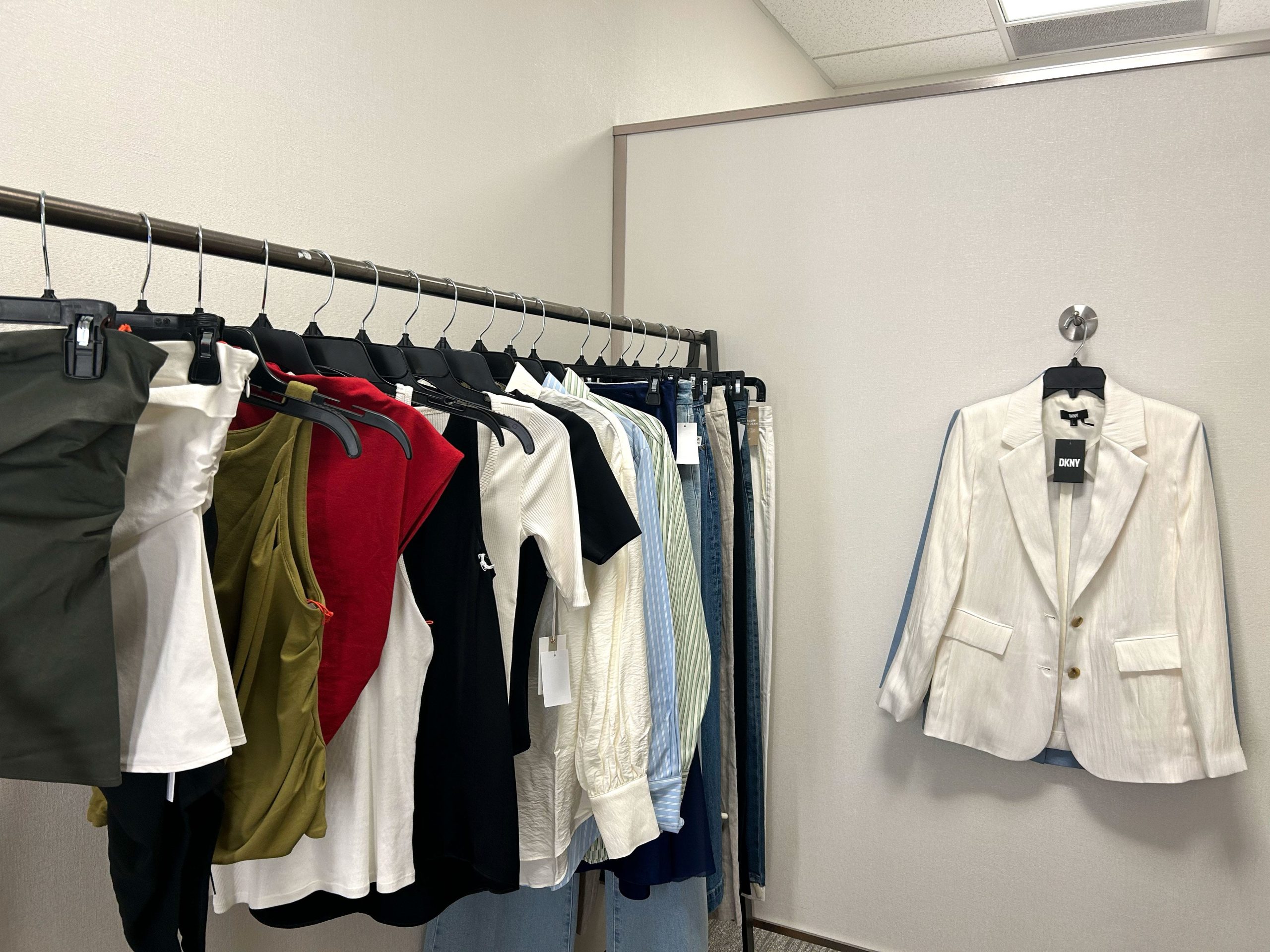 A rack of clothing and a cream DKNY blazer hanging on a hook on the wall.