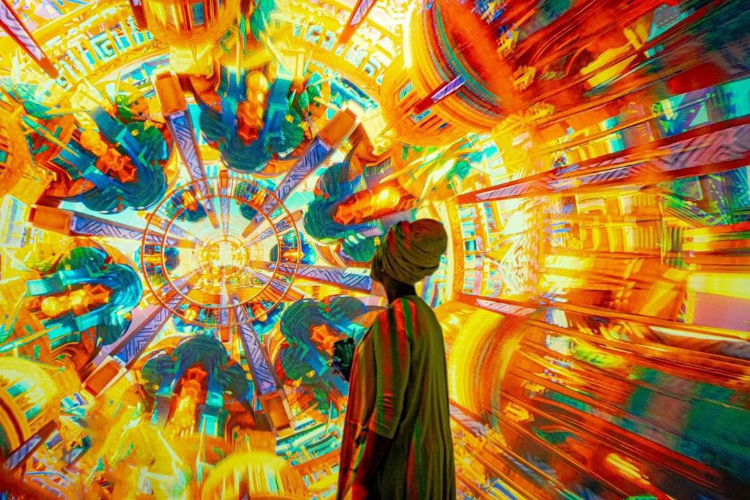 A woman looks at a digital work of art exploding with hues of yellow, orange, blue, red, and green.