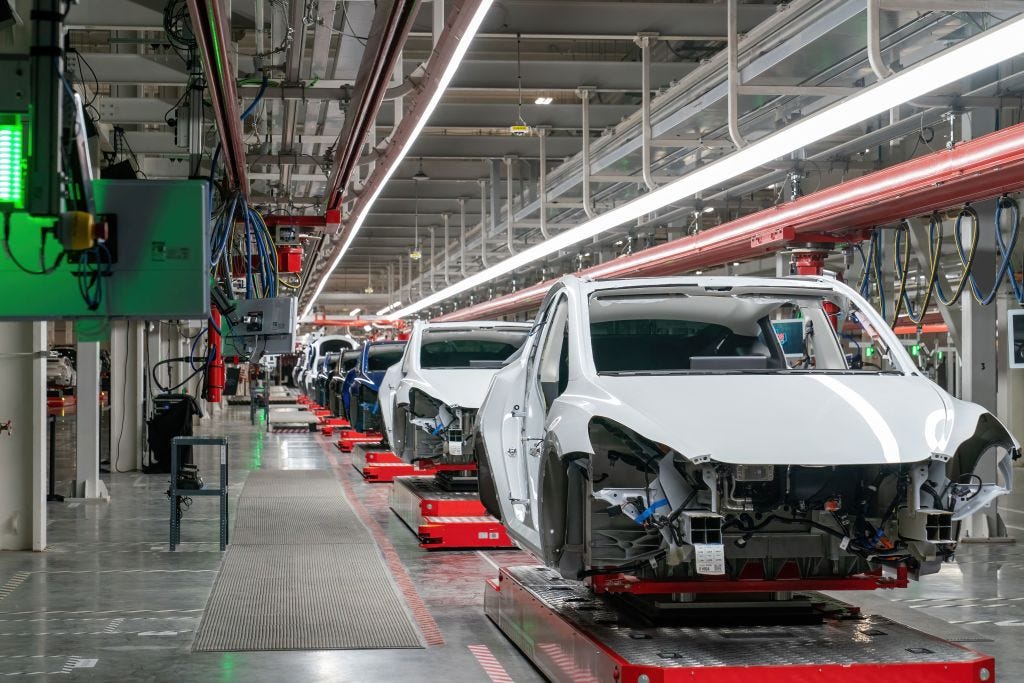 Cars frames on an assembly line in a long room.