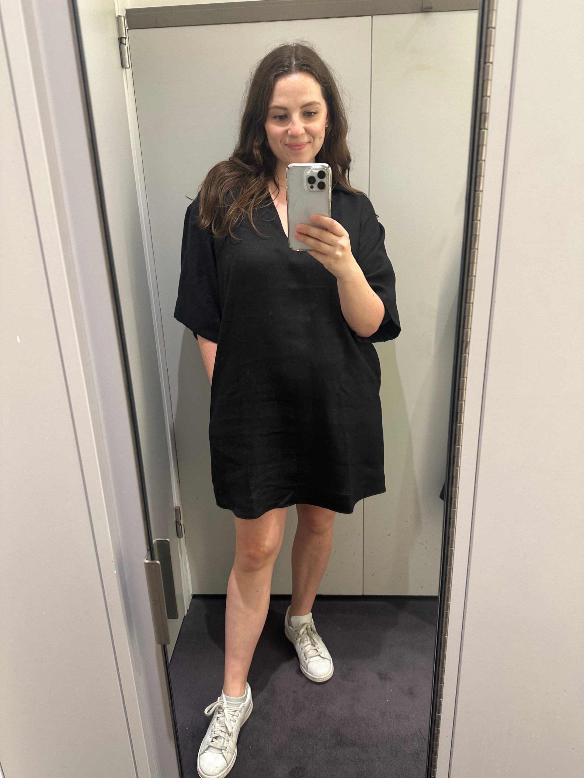 A woman takes a mirror selfie in a black dress.