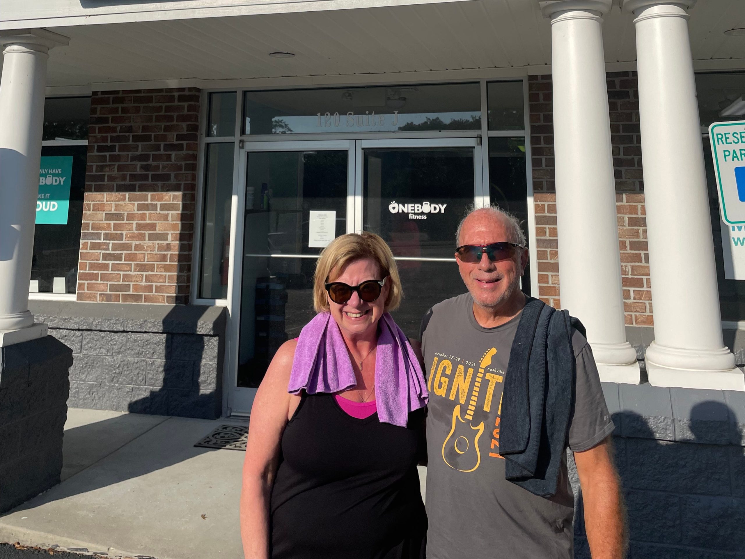 Ellen Acconcia and her husband standing in front of the gym with towels over their shoulders.