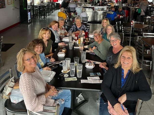 Ellen Acconcia at a big lunch table with friends, there are food and drinks on the table.