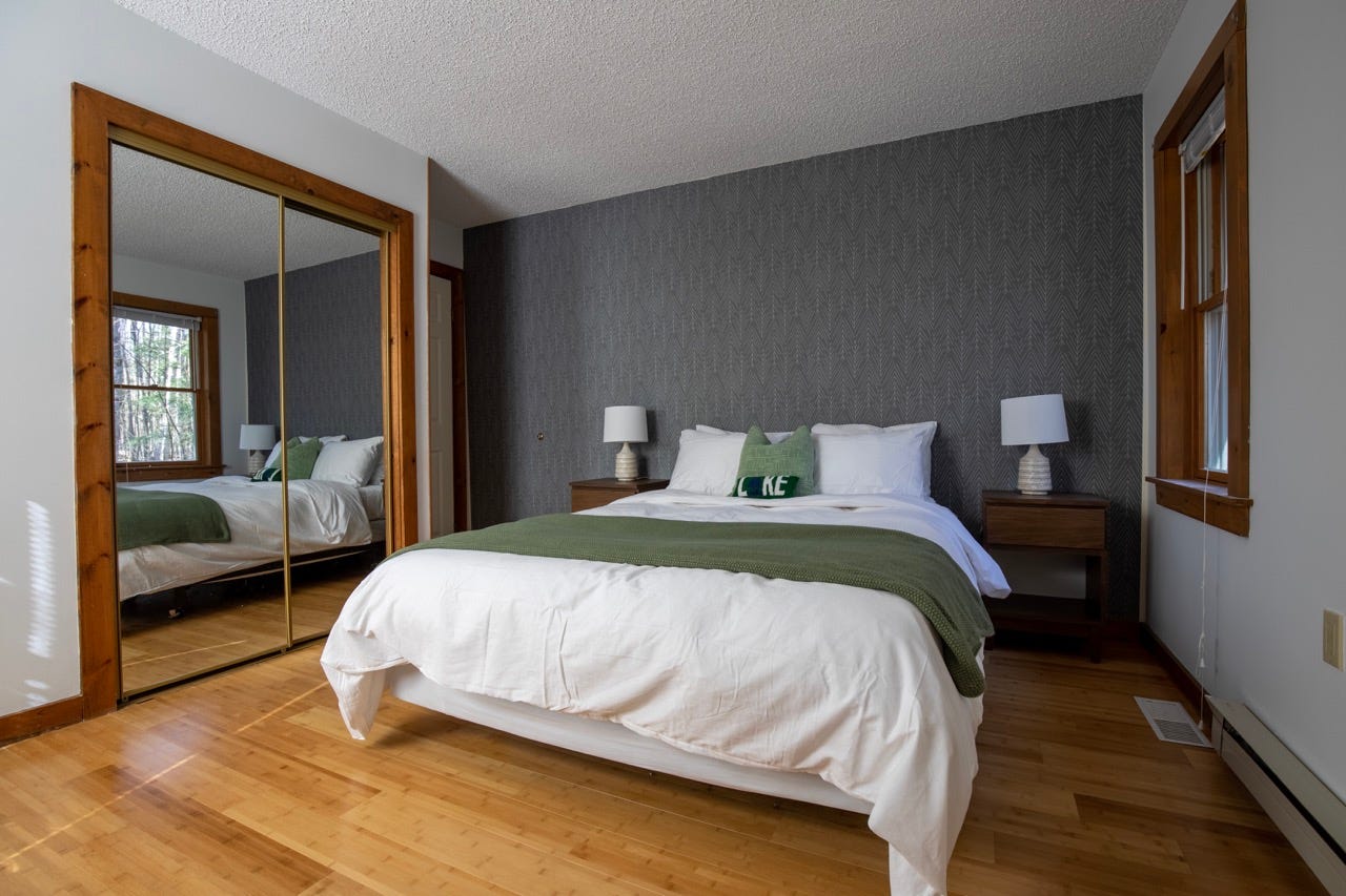 Bedroom with gray wallpaper and large bed with white linens and green accent blanket 