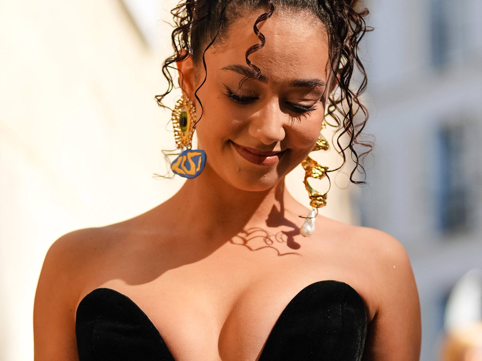 woman looking down and smiling while walking down a street wearing fancy clothes