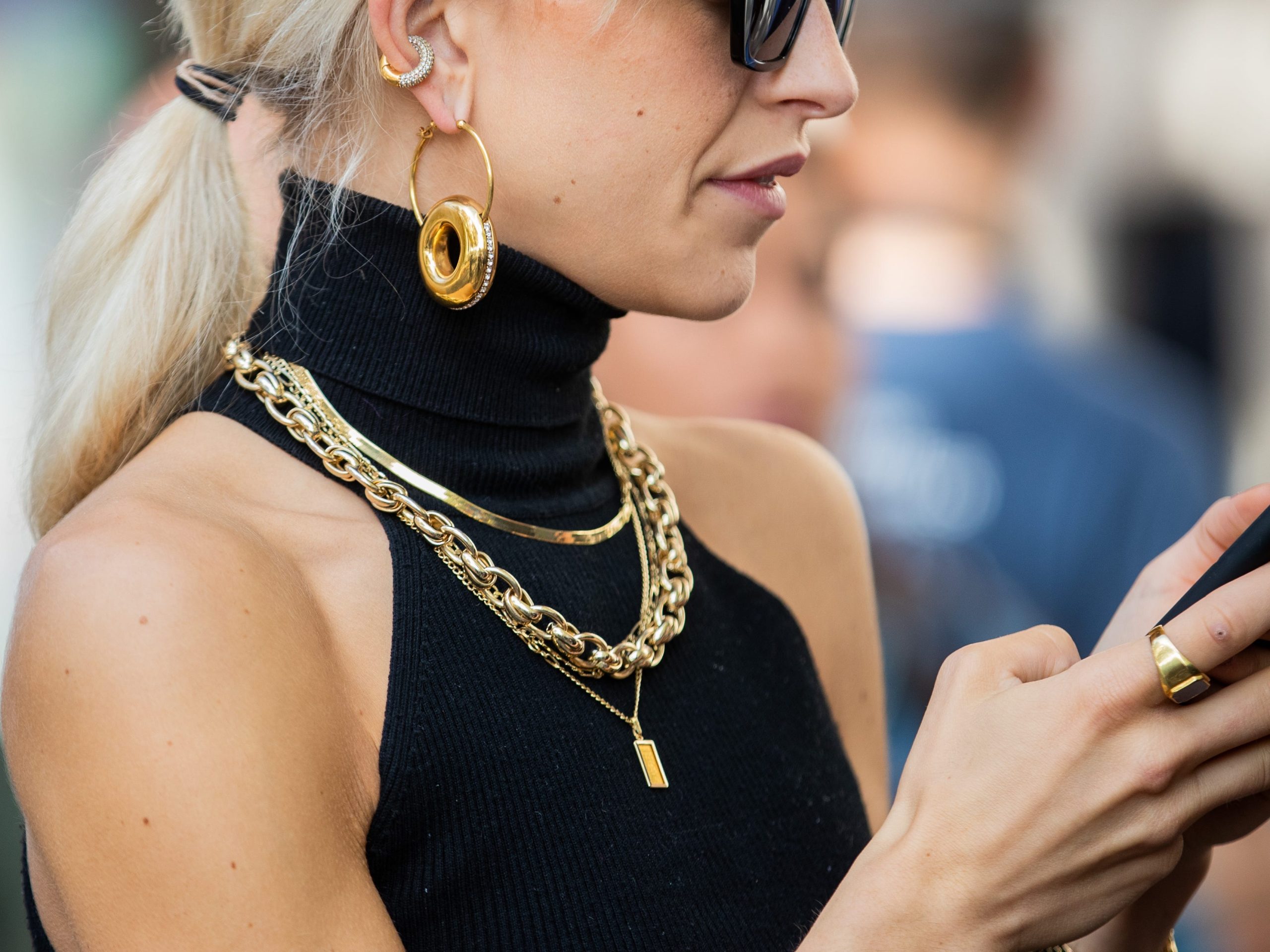 close up shot of a woman wearing gold jewelry texting on her phone while walking outside