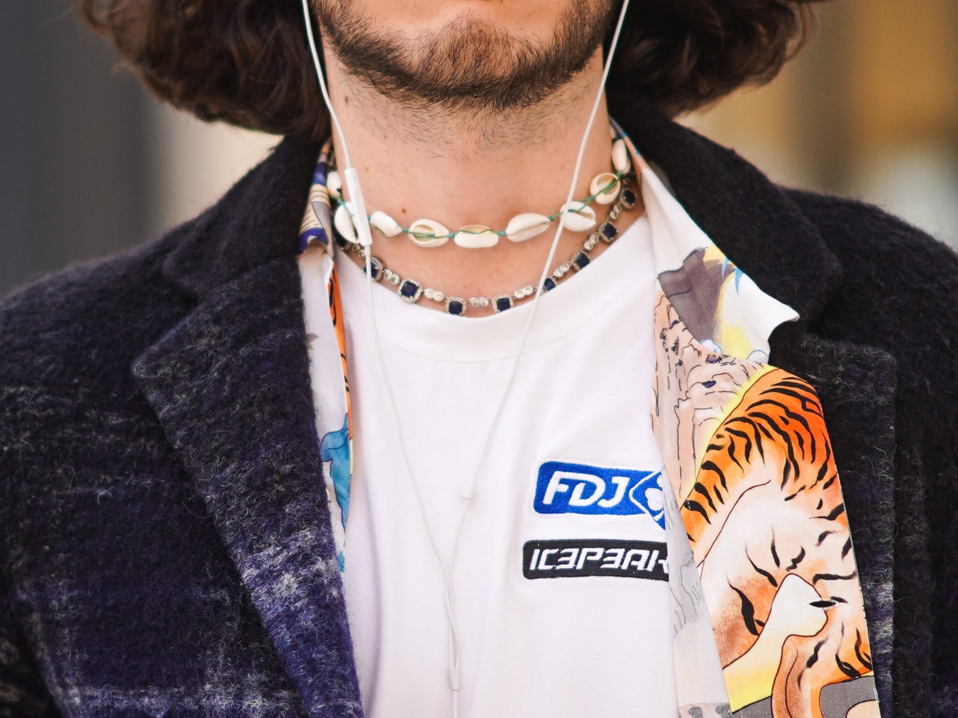 man walking down a street wearing sunglasses and earbuds with a eclectic outfit