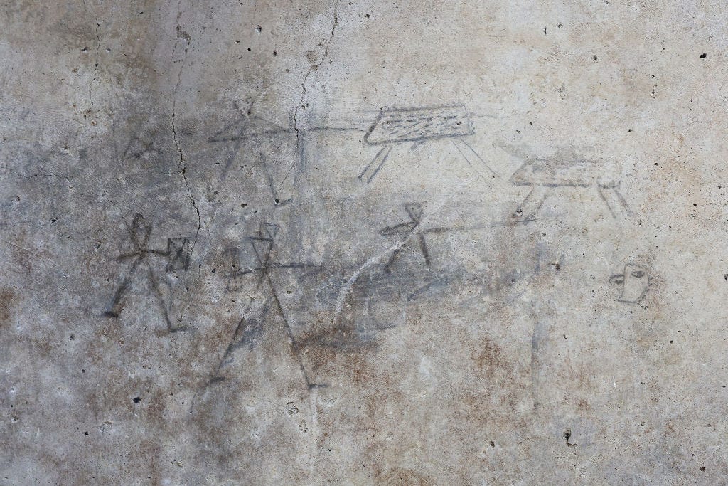 Charcoal drawings on a wall made by children showing rough images of gladiators and hunters and boar