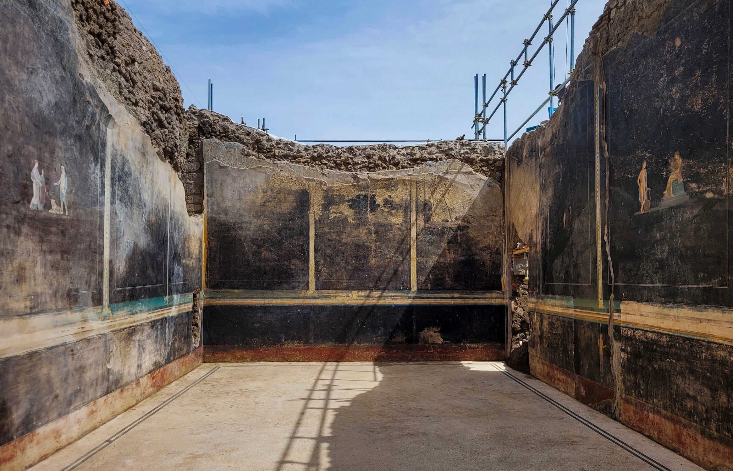 A black room in the ruins of Pompeii with frescoes on the walls and no roof