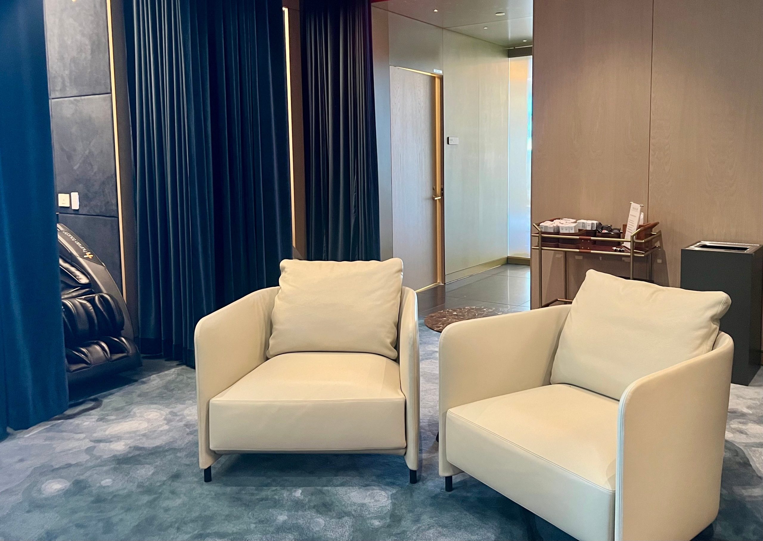 Inside the wellness center with cream chairs and a a cart in the middle of the room, and massage chair behind a blue curtain.