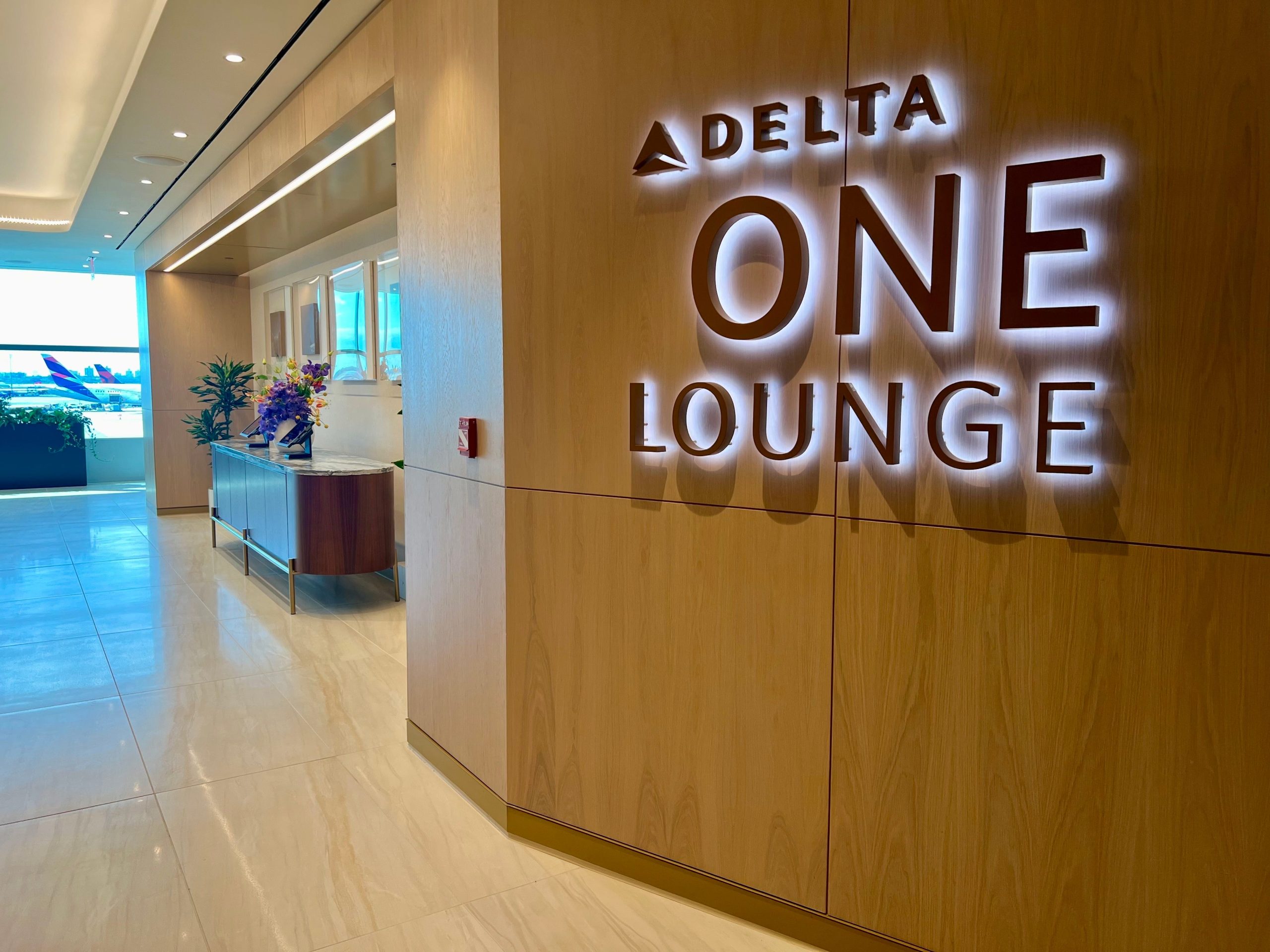 The Delta One lounge entrance sign in brown lettering with a Laram and Delta plane in background.