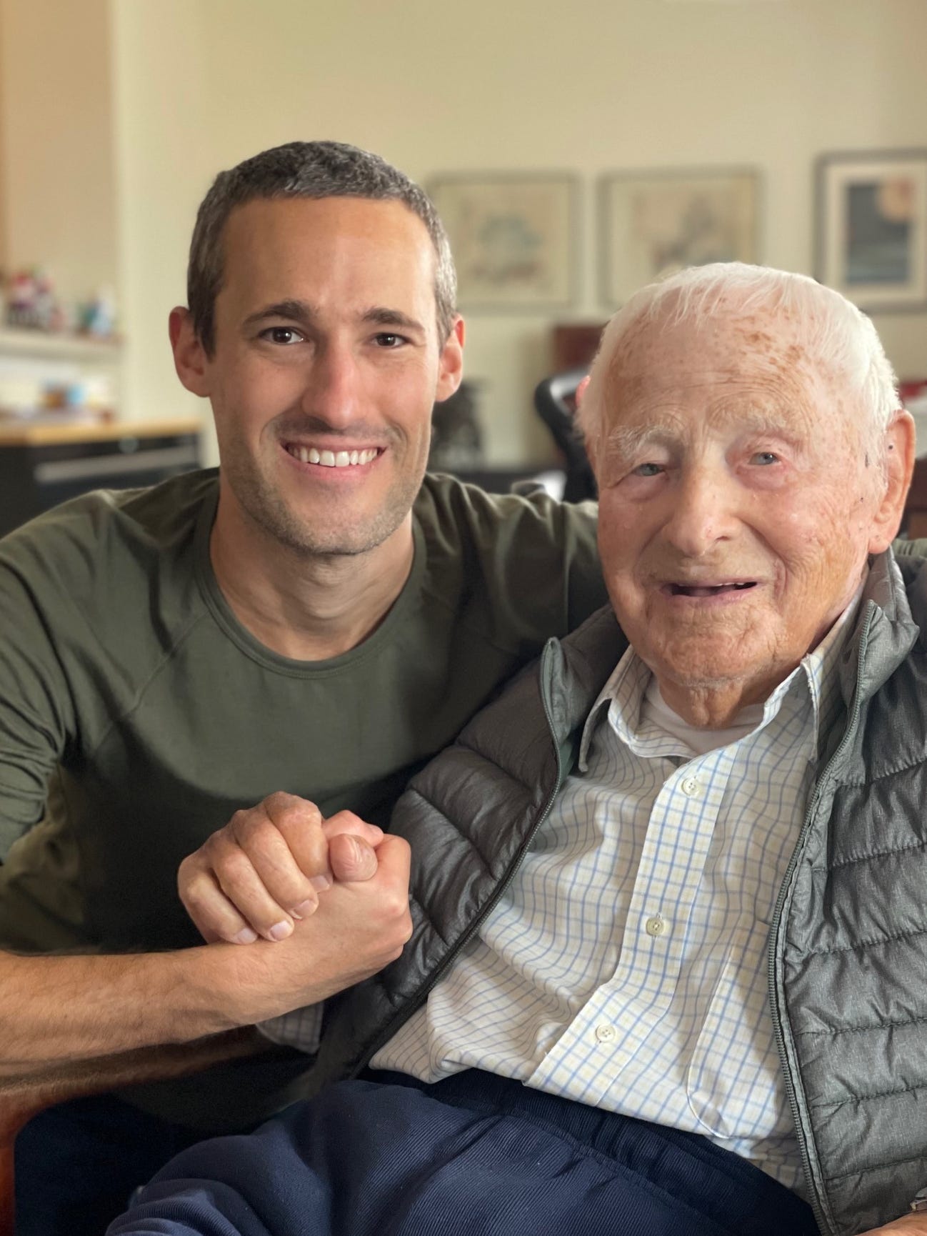 an elderly man posing for a picture with a young man, his grandson.