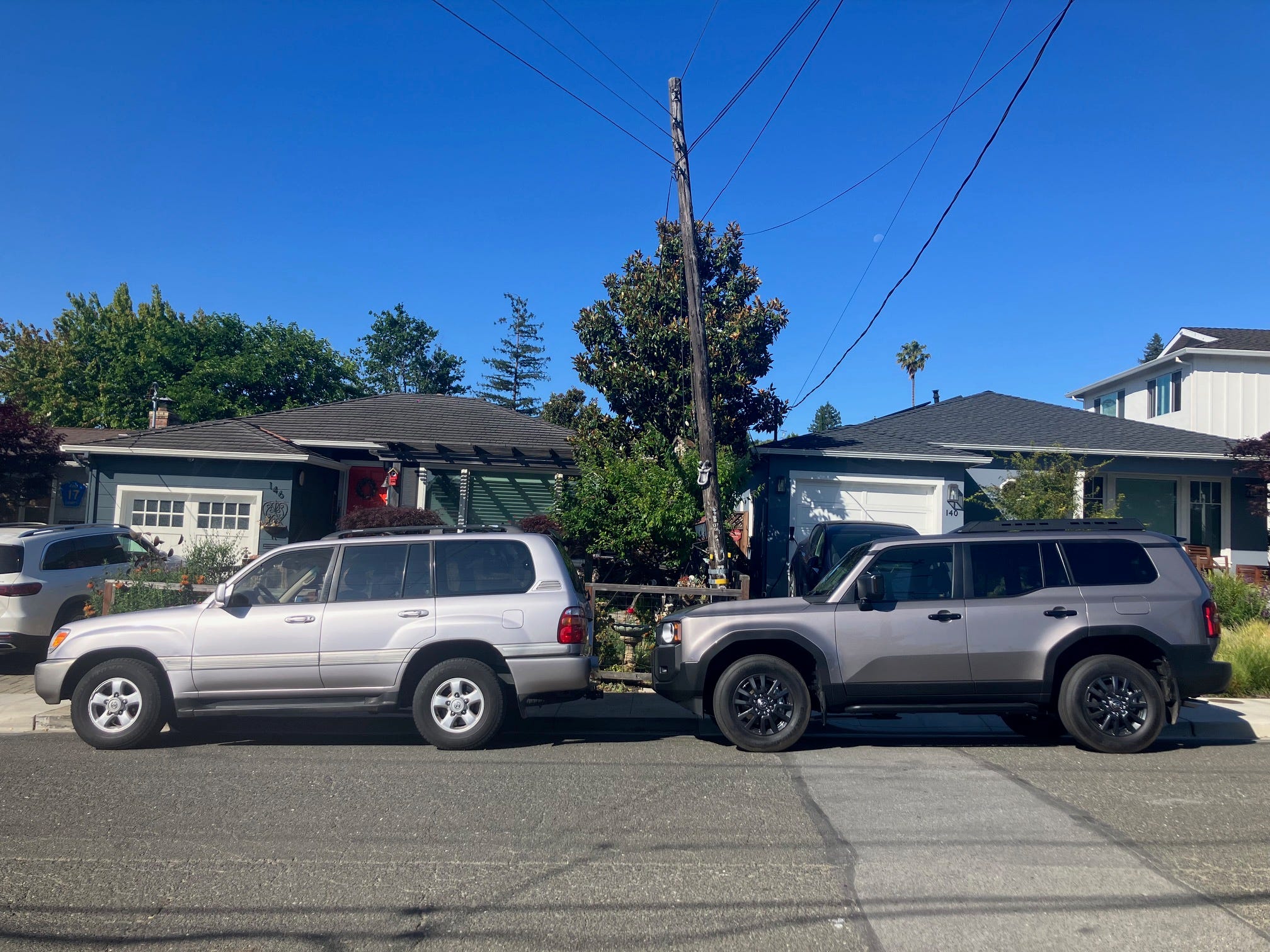 An older Toyota Land Cruiser (left) is parked on a suburban street next to a new version.