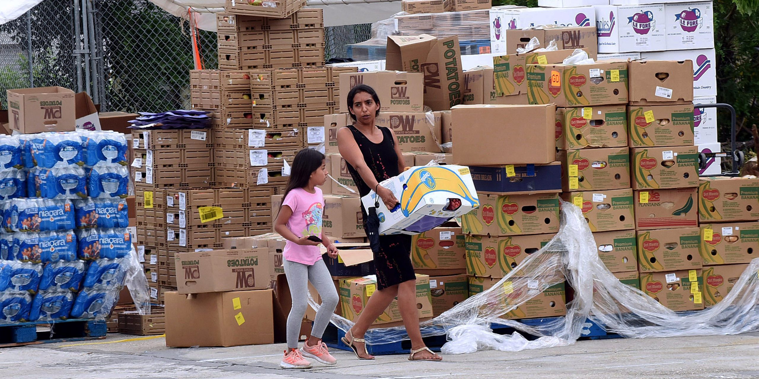 A mother and daughter carry a box of food at a food drive