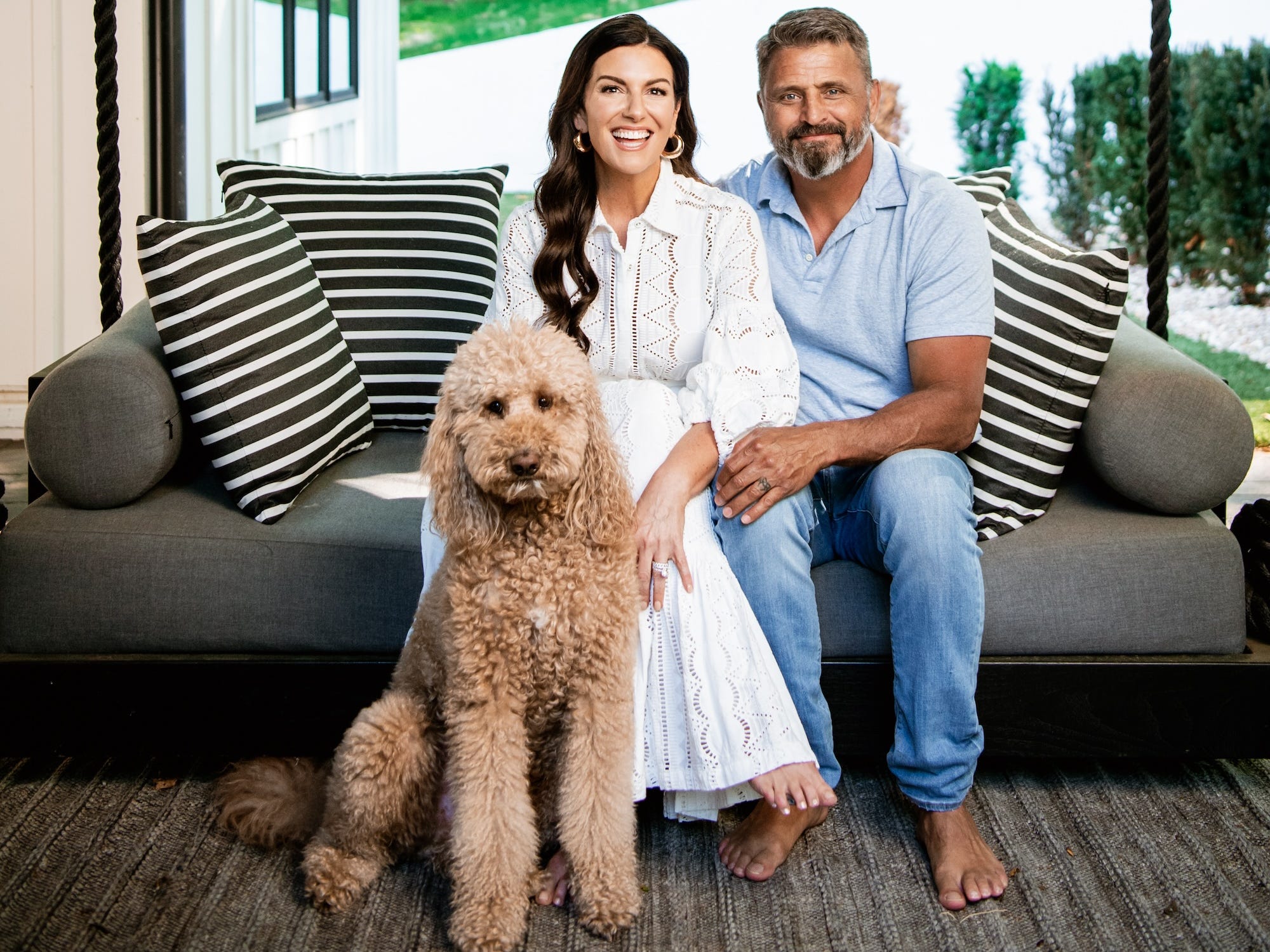 a husband and wife sit on a swing with their dog