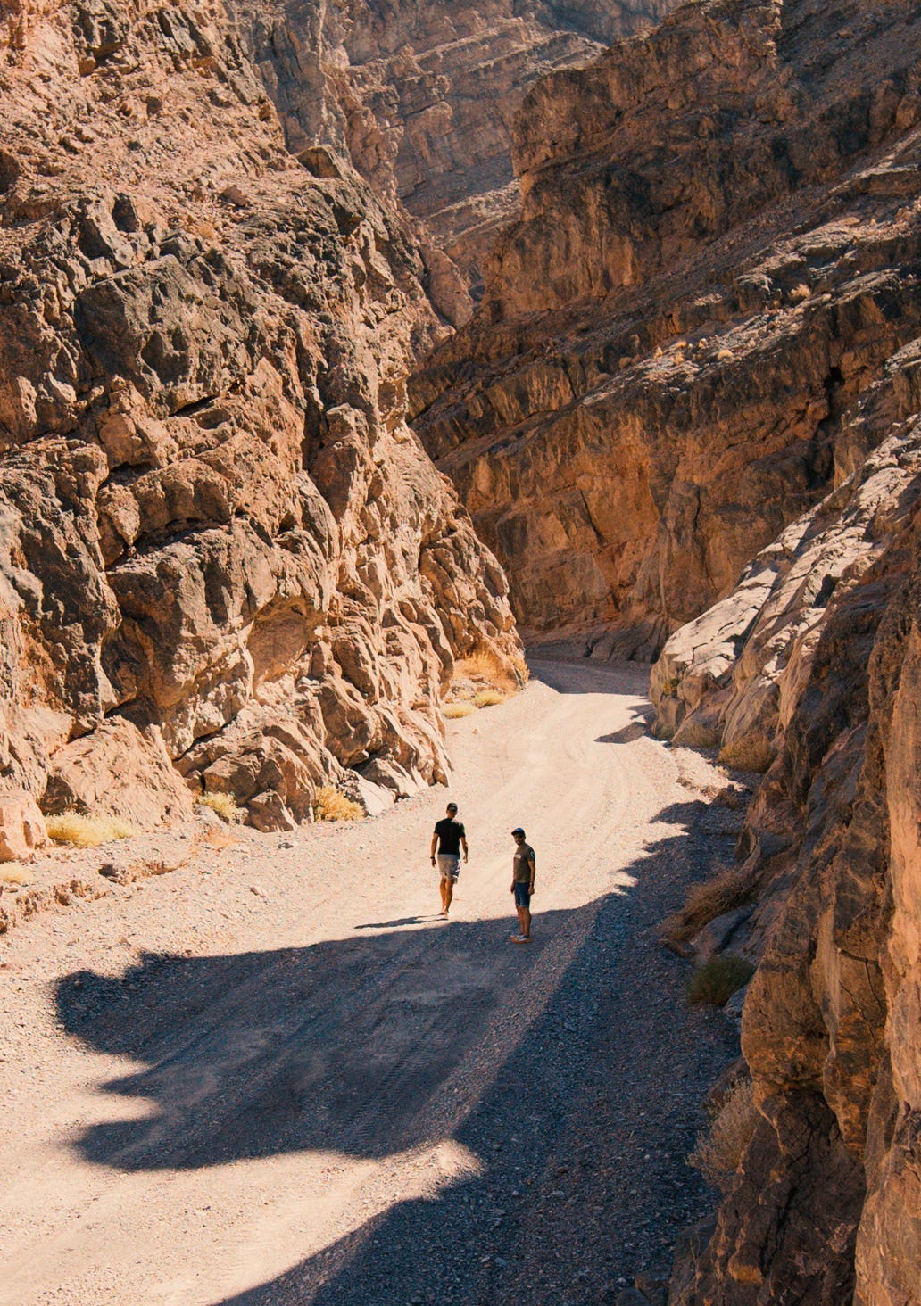 two runners standing at the bottom of a valley with massive brown rock walls on either side of them