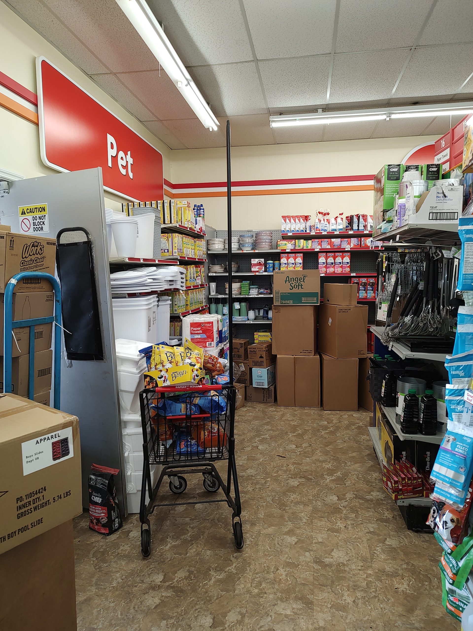 Boxes of paper goods and pet food sit on the floor and piled in a cart in the Pet section at a Family Dollar store.