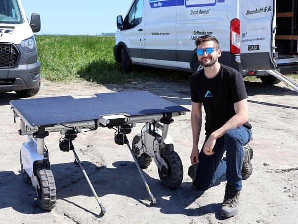 a man kneels next to a robot 